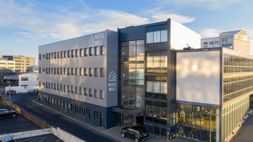 Modern exterior of Hotel Muli in Reykjavik with sleek gray facade, large windows, and a small driveway with parked cars in front.