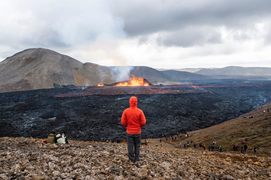 Tourists watching an active volcanic eruption with glowing lava flowing across a black lava field in Iceland.