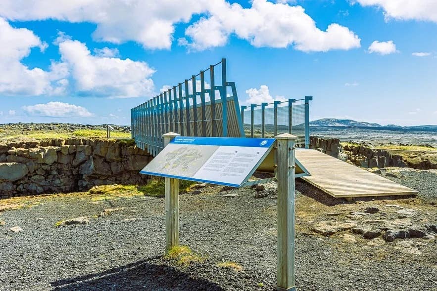 Il ponte tra i continenti in Islanda con pannello informativo e passerella in legno sotto un cielo azzurro.