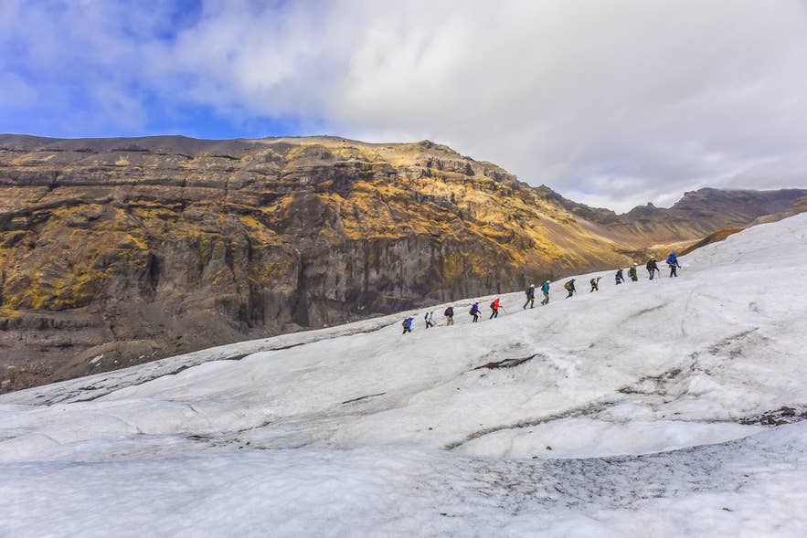 Line of hikers walking single file across a glacier with mountains behind in Southeast Iceland