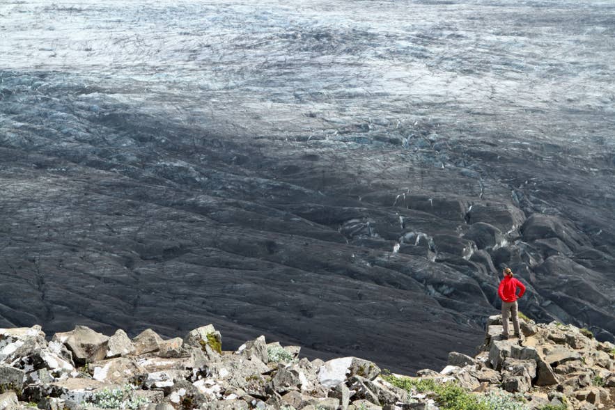 Hiker in a red jacket below the ice face of Skaftafellsjokull glacier in Skaftafell