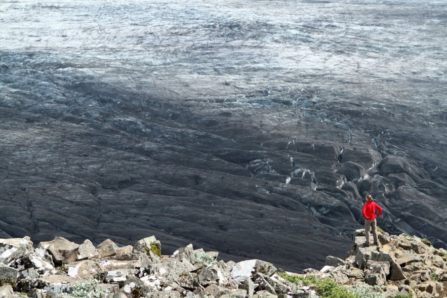 A tourist at the Sjonarnipa Viewpoint in Skaftafell is admiring a mighty glacier blackened from volcanic ash.