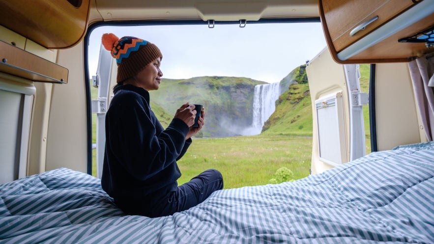 Camping in Iceland near Seljalandsfoss waterfall, traveler enjoying coffee inside a van