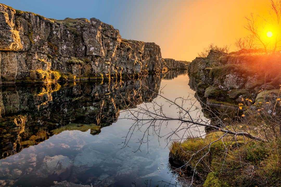 Silfra Fissure in Thingvellir National Park at sunset, with calm water reflecting moss-covered cliffs between the North American and Eurasian tectonic plates.