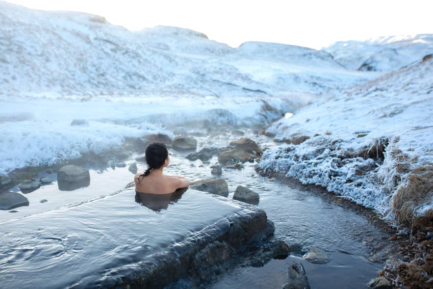Person bathing in a natural hot spring in Icelandic winter, showing nudity in Iceland and remote geothermal bathing tradition.