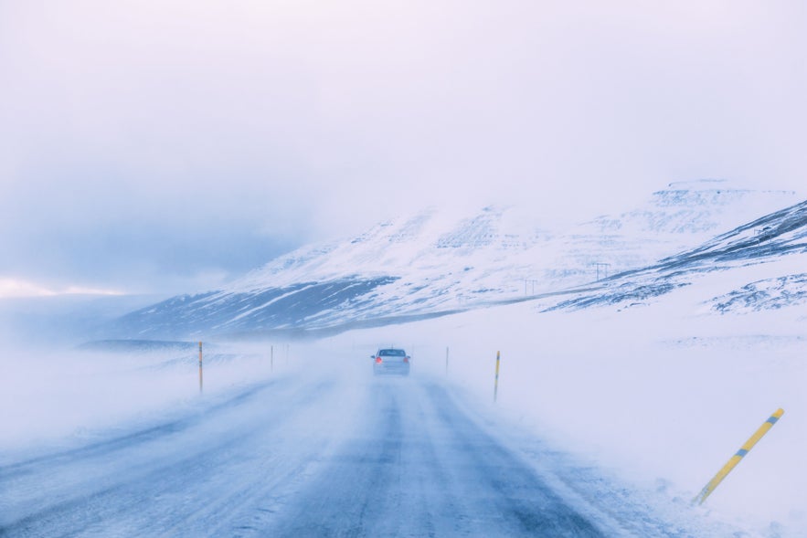 Car driving Iceland&rsquo;s Ring Road during a winter storm, showing weather risks and road safety tips for how to travel in Iceland.