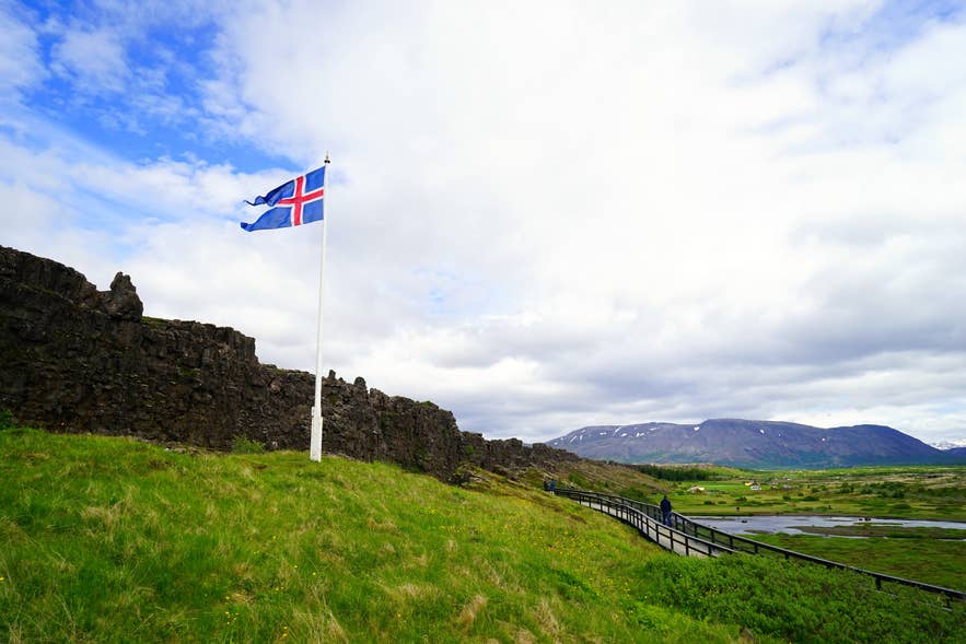 The Icelandic flag waves above the believed location of Logberg Law Rock, set between the Almannagja Gorge and grassy surroundings.