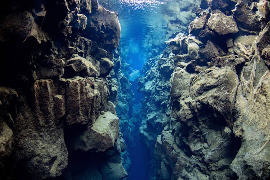 Silfra Fissure reveals clear blue water flowing between rugged rocks.