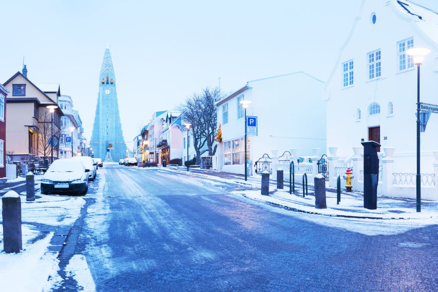 Winter street in Reykjavik with Hallgrimskirkja church rising above snow-covered houses and a quiet icy road.