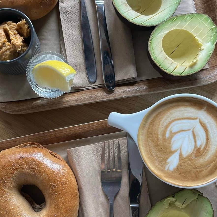 Ontbijt met bagels, avocado, citroen, hummus en een latte op houten dienbladen, geserveerd in een knus café in IJsland.
