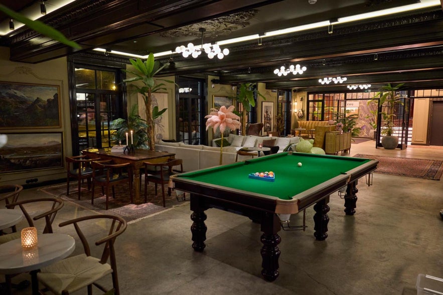 Hotel Akureyri lounge interior with a billiards table, cozy seating areas, warm lighting, and plants creating a relaxed atmosphere.