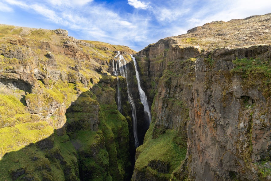 Glymur Waterfall in Iceland surrounded by green hills and flowing river during summer.