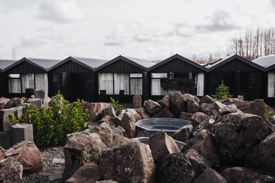 Modern hotel cabins and outdoor hot tubs at a geothermal spa near Fludir in South Iceland, surrounded by volcanic rock.