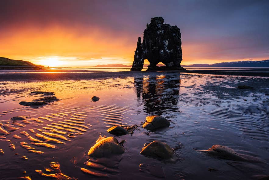 Spektakulärer Sonnenuntergang am Felsen Hvitserkur auf der Vatnsnes-Halbinsel in Island mit leuchtenden Spiegelungen am Ufer bei Ebbe.