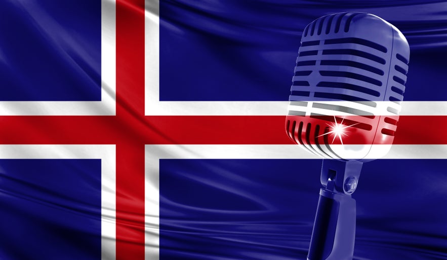A classic silver studio microphone positioned in front of a waving national flag of Iceland, symbolizing the country&rsquo;s rich musical heritage and Eurovision legacy.