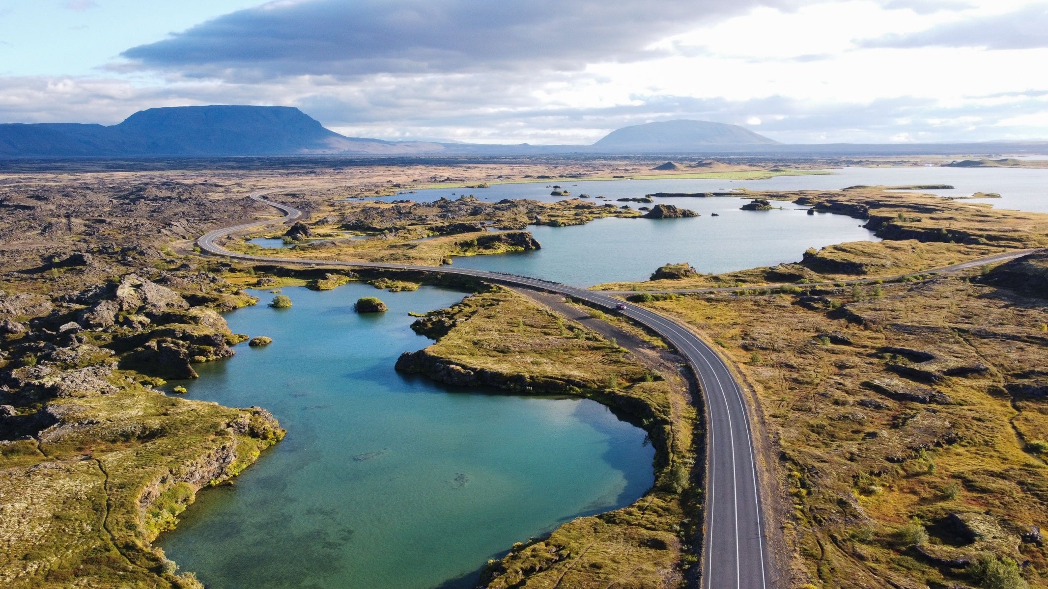 アイスランドの溶岩原にある曲がりくねった道路とターコイズブルーの湖の空撮。アイスランド地図によく登場する風景。