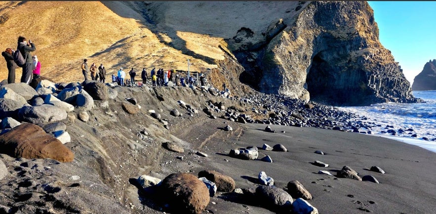 Reynisfjara eroded shoreline with exposed slope, scattered boulders, and visitors observing the damage, photo by J&oacute;nas Erlendsson.
