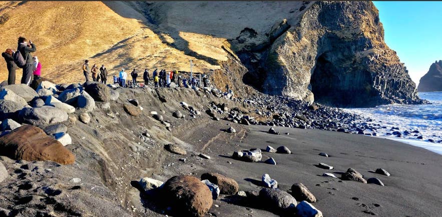 Reynisfjara eroded shoreline with exposed slope, scattered boulders, and visitors observing the damage