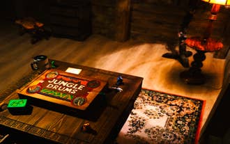 Jungle Drums board game box on a wooden table with dice and pieces in a cozy, dimly lit room.