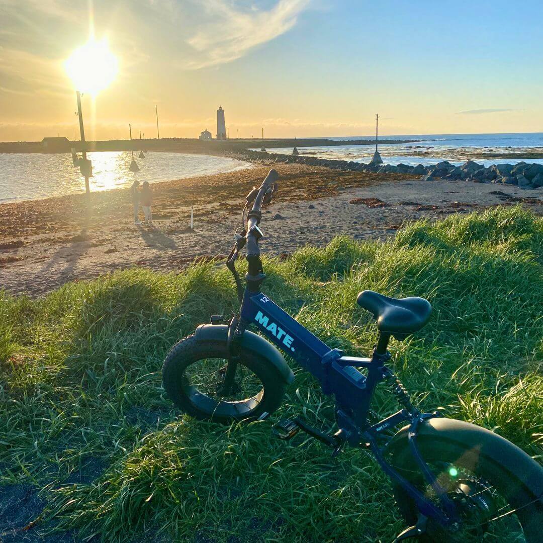 E-bike resting on a grassy coastal trail in Reykjavik with ocean views and soft sunset light over the shoreline