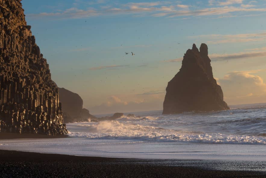 Basalt columns and Reynisdrangar sea stack at Reynisfjara beach with waves crashing at sunset in South Iceland.