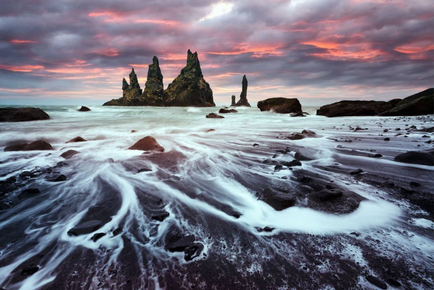 Sunset at Reynisfjara Black Sand Beach in Iceland with waves washing over black sand and basalt sea stack rock formations.