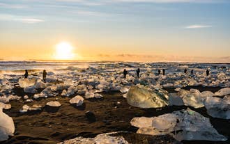 Diamond Beach at sunset with ice chunks scattered across black sand and visitors walking along the shoreline.