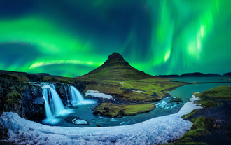 Kirkjufell mountain and Kirkjufellsfoss waterfall under bright northern lights on the Snæfellsnes Peninsula in Iceland.
