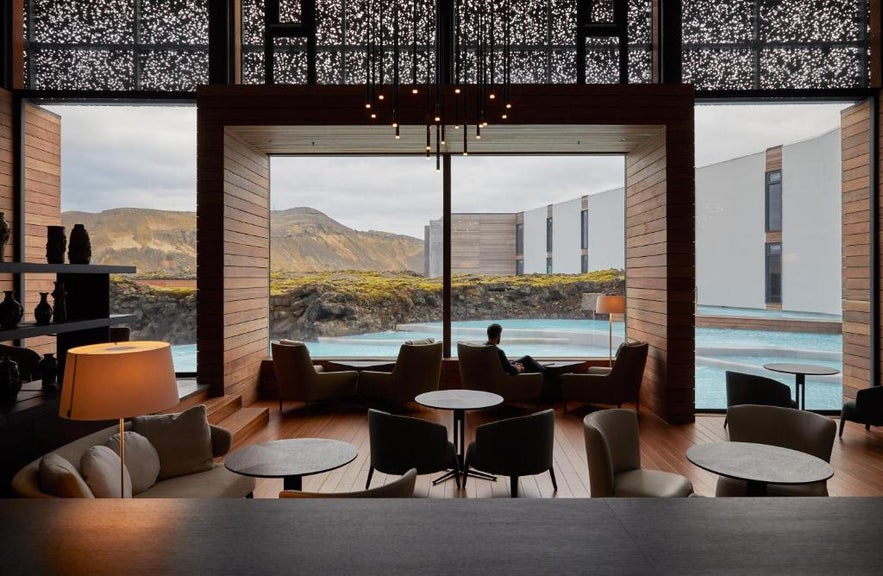 The interior lounge of The Retreat at Blue Lagoon, featuring floor-to-ceiling windows, minimalist wood paneling, and views of volcanic lava fields.