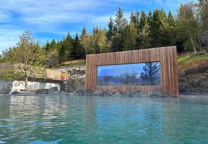 Contemporary sustainable design of the Forest Lagoon in Akureyri, featuring vertical wood cladding and a large reflective window integrated into a cliffside forest.