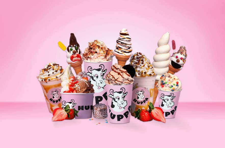 Colorful Huppa Iceland ice cream cups and cones topped with candies, cookies, and sauces against a pink background.