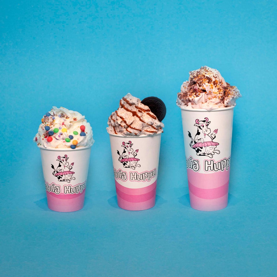 Three mix-in ice creams from &Iacute;sb&uacute;&eth; Huppu in branded cups with creamy toppings against a blue background