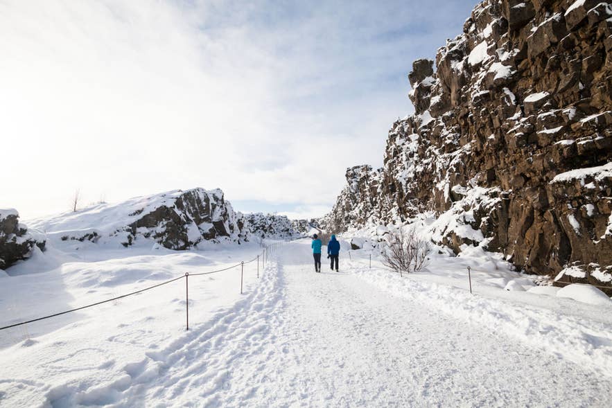 Two visitors walk through the snow-covered Almannagja Gorge in Thingvellir National Park.