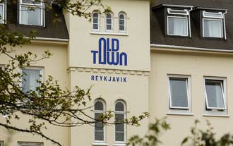 Old Town Reykjavik exterior with cream façade and blue sign surrounded by trees.
