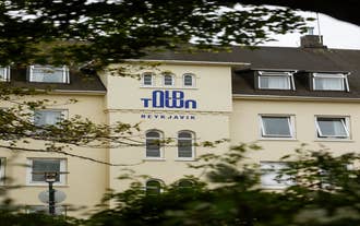 Old Town Reykjavik exterior with cream façade and blue sign surrounded by trees.