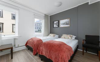 Bright twin room at Old Town Reykjavik with grey wall, large window, and red blankets.