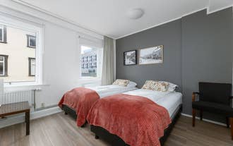 Bright twin room at Old Town Reykjavik with grey wall, large window, and red blankets.