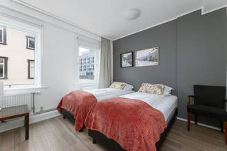Bright twin room at Old Town Reykjavik with grey wall, large window, and red blankets.