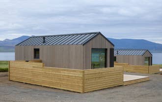 The exterior of a modern wooden cabin with a private hot tub terrace at Eyri Farm.