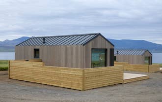 The exterior of a modern wooden cabin with a private hot tub terrace at Eyri Farm.