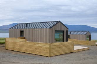 The exterior of a modern wooden cabin with a private hot tub terrace at Eyri Farm.