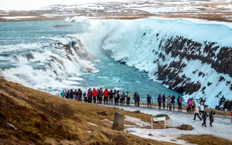 A group of people views Gullfoss Waterfall as icy turquoise water crashes into the canyon on a private Golden Circle tour.