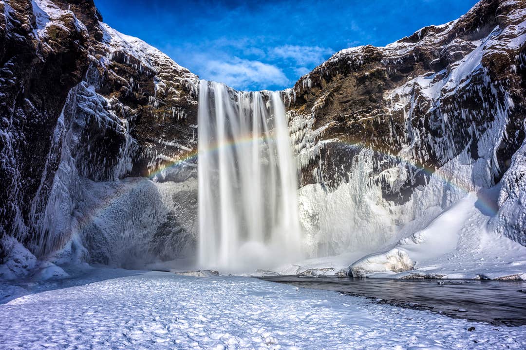 Skogafoss Waterfall cascading over a cliff in winter with snow-covered ground.
