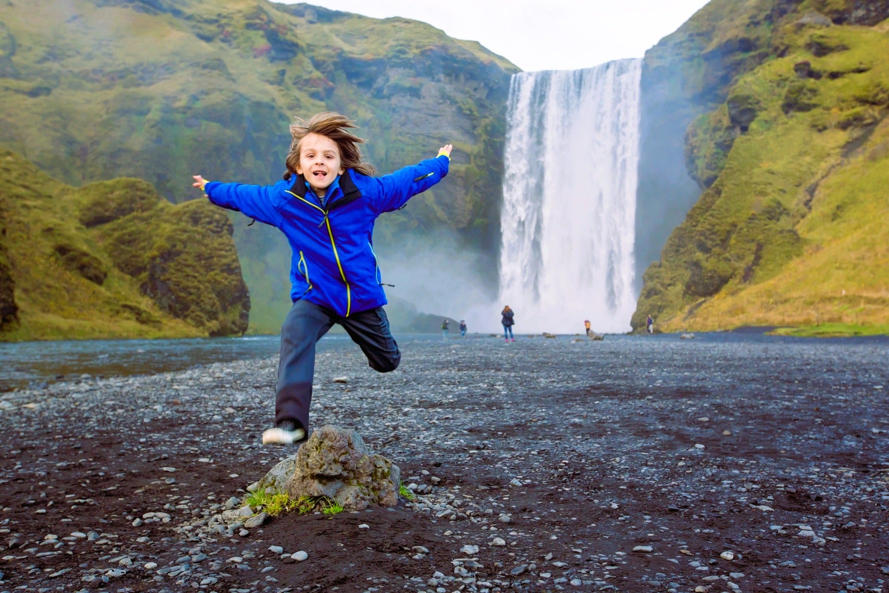 Kind spelend op het zwarte zand bij de waterval Skogafoss aan de Zuidkust, ideaal voor IJsland met kinderen.