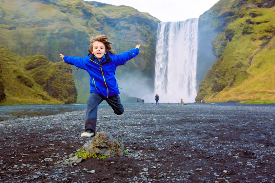 Bambino che gioca sulla sabbia nera alla cascata Skogafoss sulla Costa sud, perfetto per un viaggio in Islanda con bambini.
