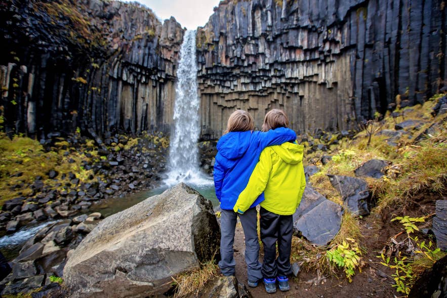 Islanda con bambini che esplorano la cascata Svartifoss nel Parco Nazionale di Vatnajokull, circondati da colonne di basalto.