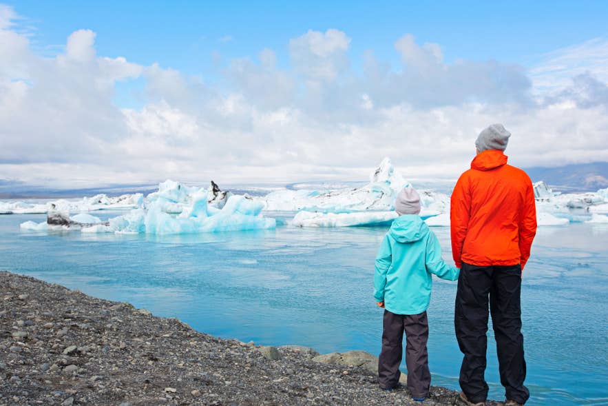 Island med barn ved Jokulsarlon isbrelagune på sørkysten, ser på drivende blå isfjell sammen.