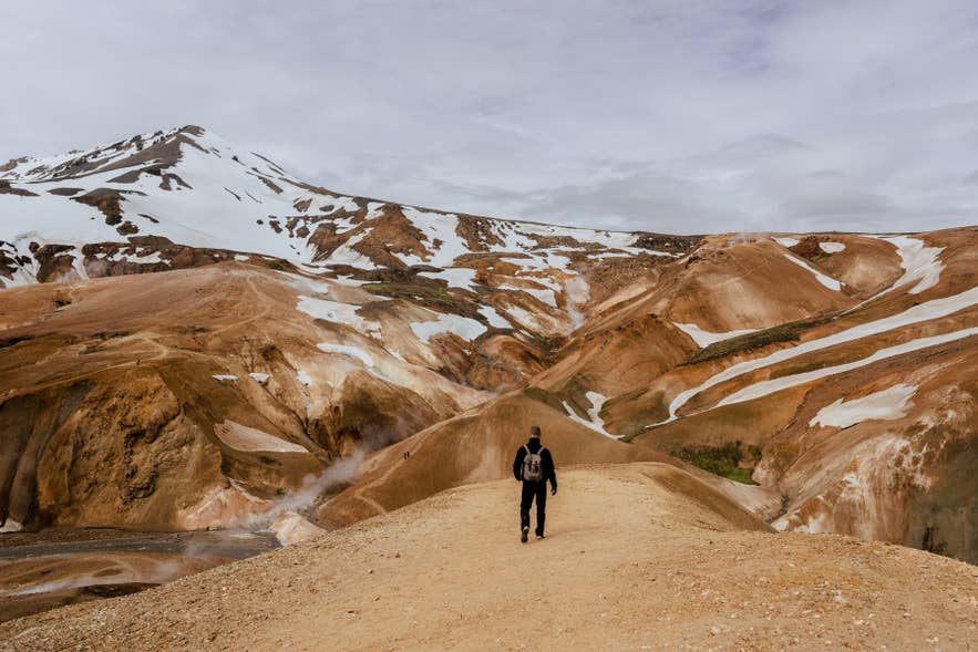 Viajero de pie en las Tierras Altas de Landmannalaugar con montañas de riolita cubiertas de nieve, un paisaje habitual en los mapas de Islandia.