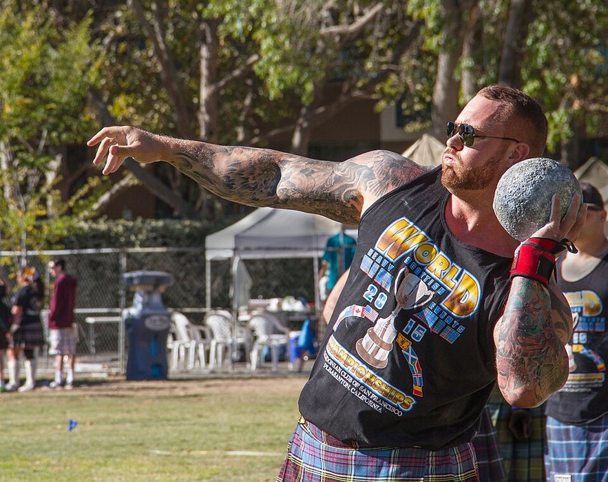 Hafthor Julius Bjornsson wearing sunglasses and a kilt prepares to throw a heavy stone during a Highland Games competition outdoors.