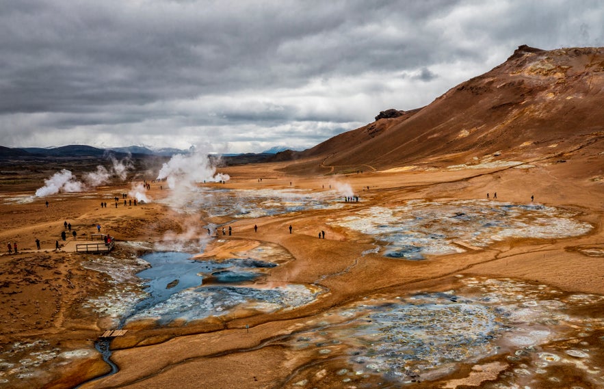 Hverir Geothermal Area in North Iceland with steaming fumaroles, bubbling mud pools, and colorful mineral deposits under dramatic cloudy skies.